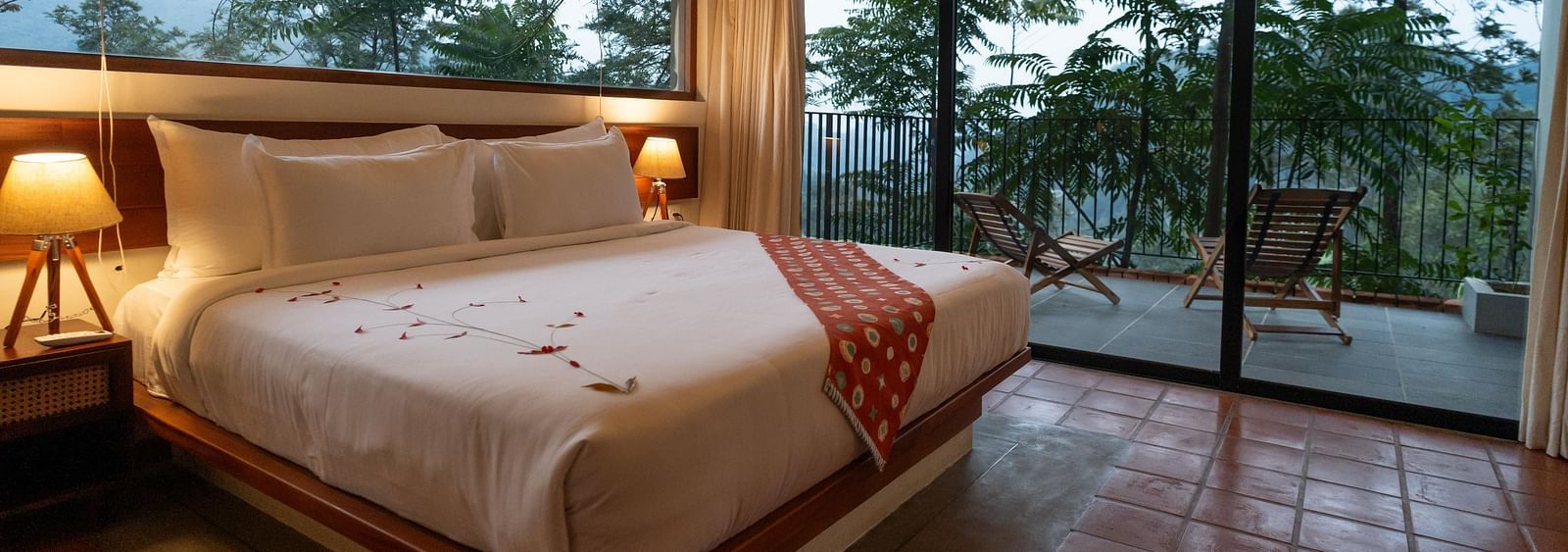  A well-appointed bedroom at Vaasta Vagamon featuring a large bed with a decorative runner, and expansive windows overlooking a scenic view.