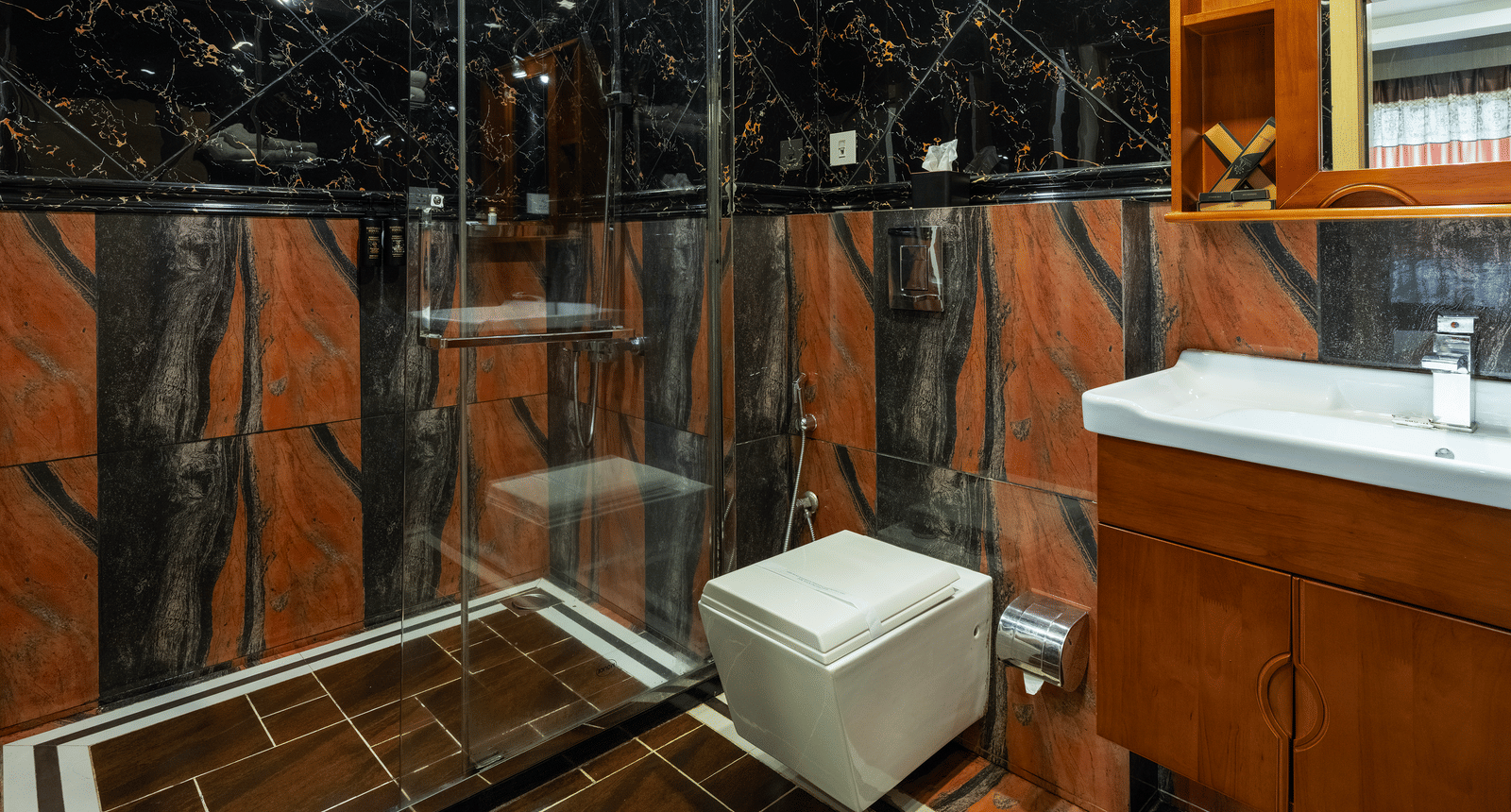 A modern bathroom of the Premium Room at Parakkat Nature Hotel and Resorts, Munnar featuring high-gloss, patterned wall tiles, a sink vanity, storage, and a shower area.