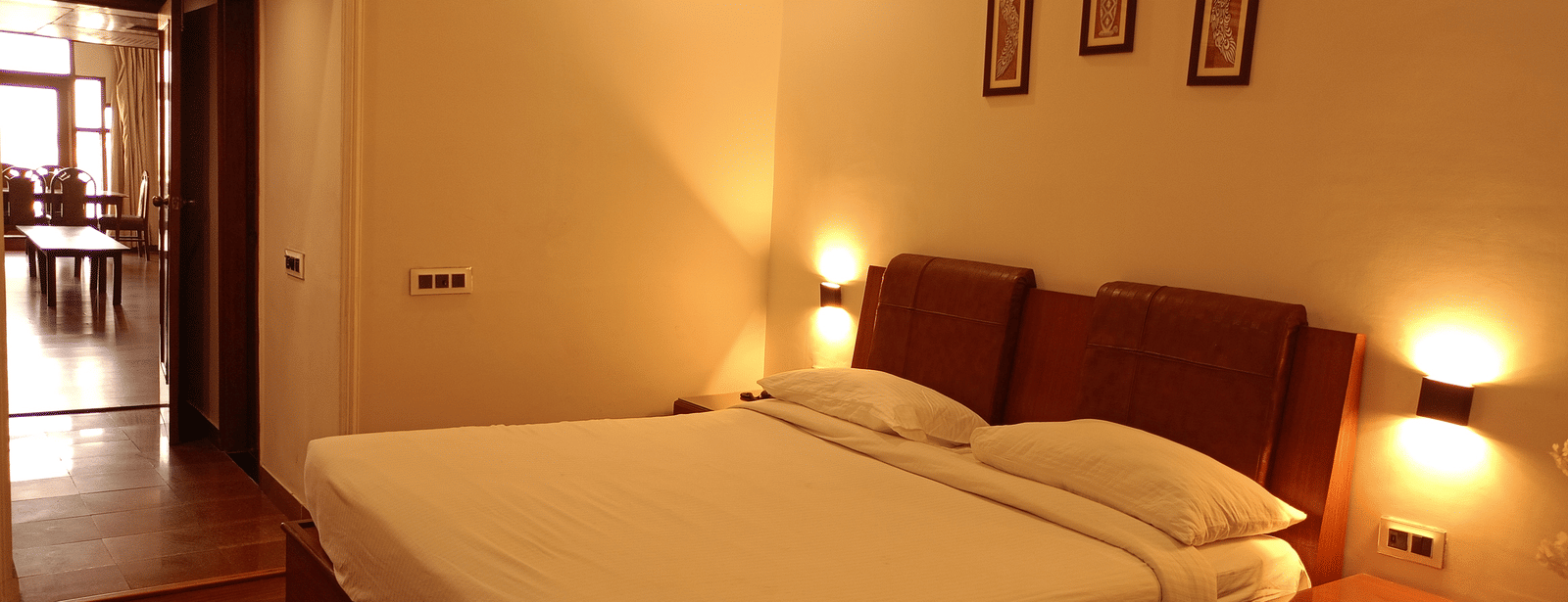 Guest room at Hotel Gold, Panipat featuring a bed, side tables, and framed wall art.