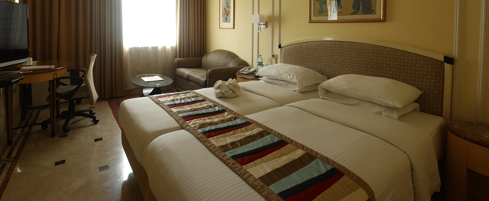 Twin beds in the Superior Room with sunlight peeking through the windows at Regency Hotel, Mumbai.