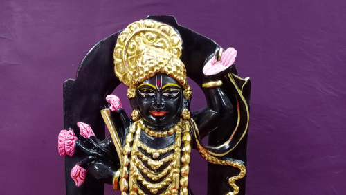 A beautiful black marble idol of the Hindu god Krishna, adorned with a golden crown, jewellery, and pink flowers.