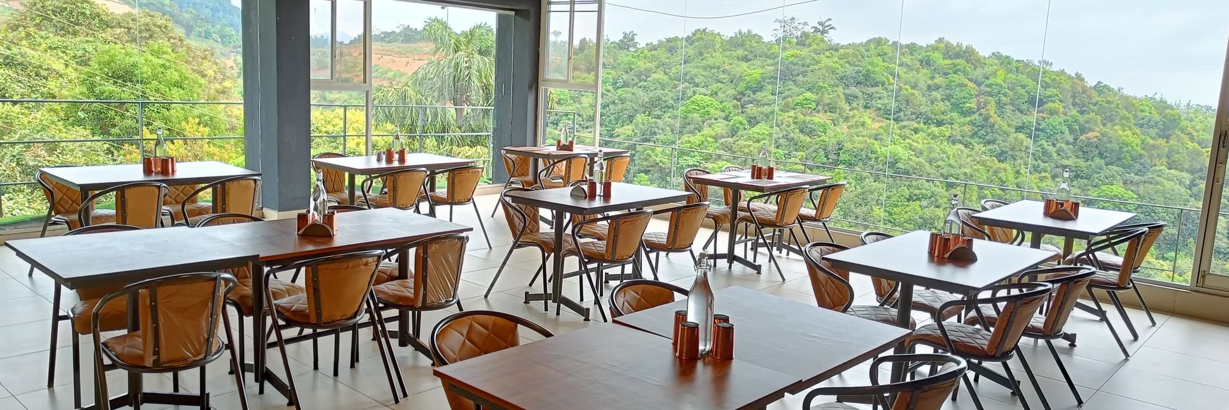 Open-air dining area with wooden tables and scenic hill views at The Cliff Edge Coorg Hotel.