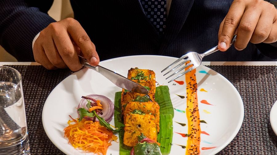 Person cutting into a plated dish featuring grilled skewers and side accompaniments.
