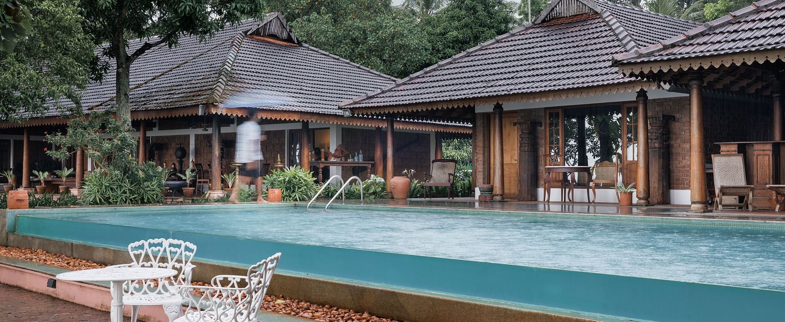 A shot of the pool with chairs and table near it and the restaurant in the background - BluSalzz Villas - Muhamma Resort, Alleppey