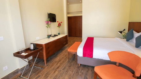 A room with a bed, orange chairs, and a wooden television stand with a kettle at Estherea Elite, Morjim.