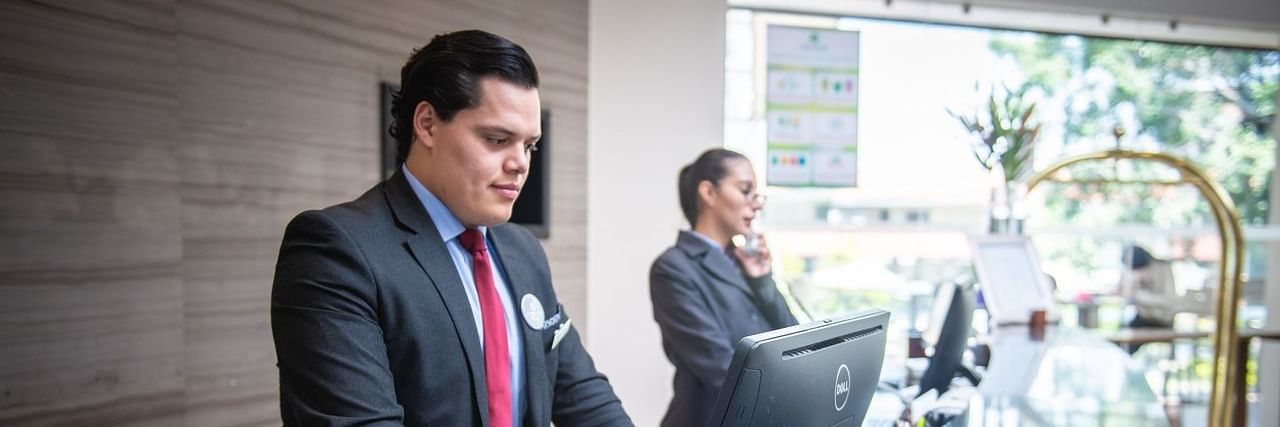 Two staff members standing behind the reception desk looking at the computer in front of them.
