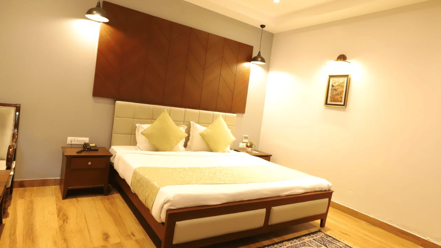 A bedroom with a king size bed, wood headboard panel, nightstand, and pendant lights at Amantra Shilpi Resort, Udaipur.