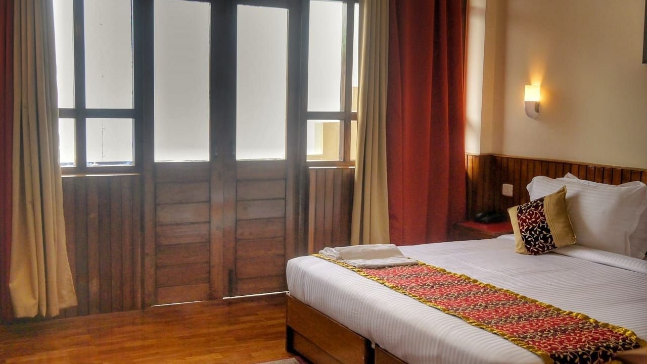 An image of the super deluxe room at Ecotel Chiminda, Pelling featuring a queen size bed, and an expansive door leading to the balcony