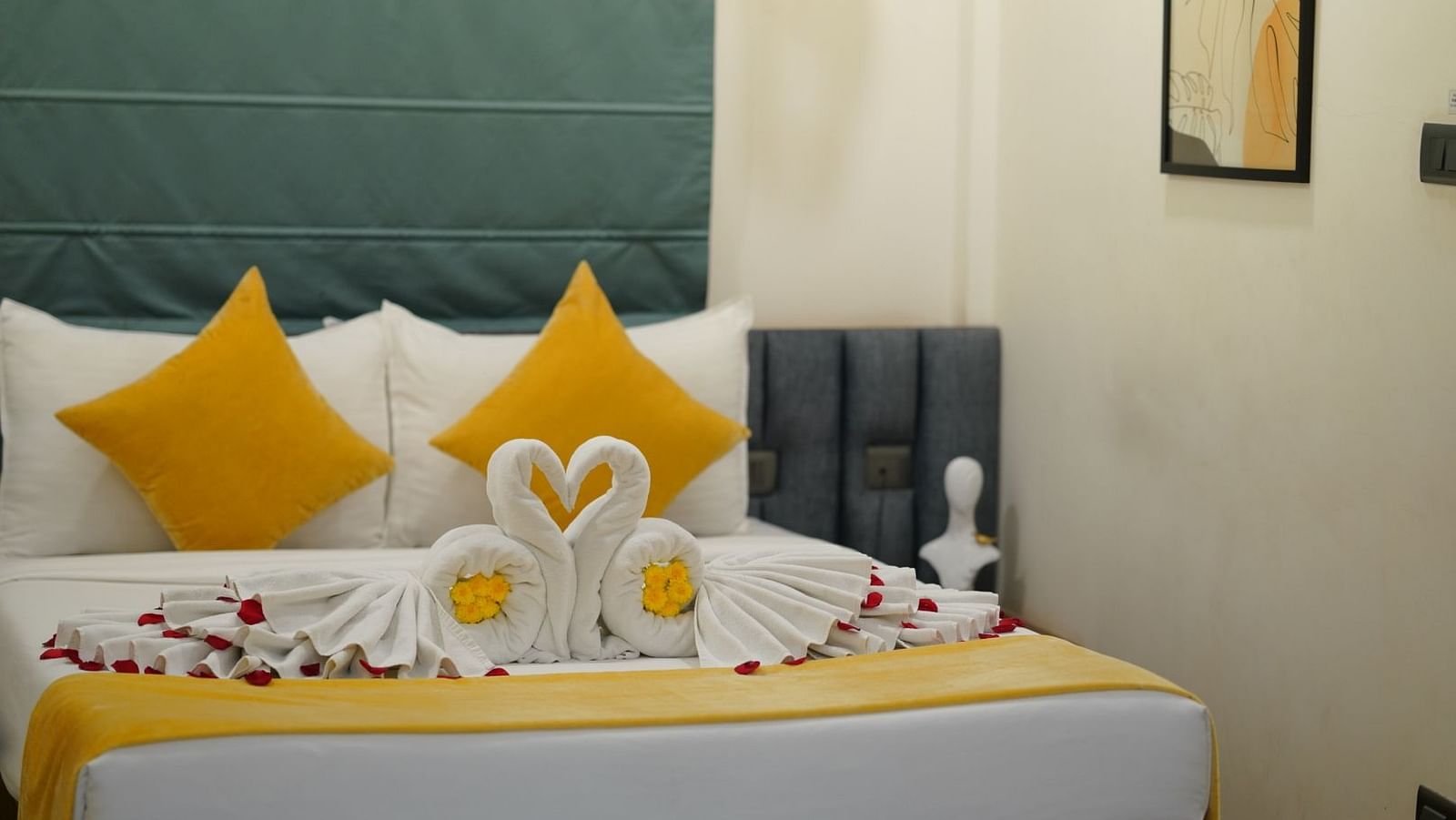 A room with a neatly made double bed adorned with yellow and towels shaped into swans, scattered with rose petals for a welcoming touch at Kyzen Smart Stays.