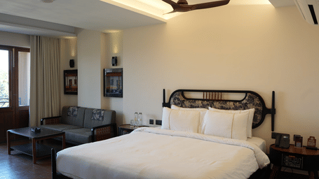 A bedroom featuring a double bed with white sheets, a grey sofa, and a ceiling fan at Hotel Sonar Bangla, Ajodhya Hills.