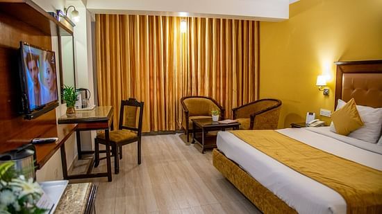 A full view of a room with a bed, TV, writing desk, coffee table and chairs | Sun Park Hotel & Banquet, Chandigarh - Zirakpur