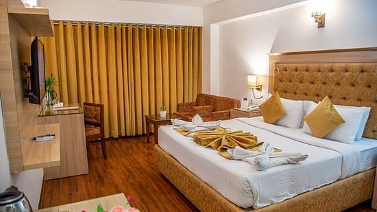 A bed with bedding in a room with a writing desk and a TV | Sun Park Hotel & Banquet, Chandigarh - Zirakpur
