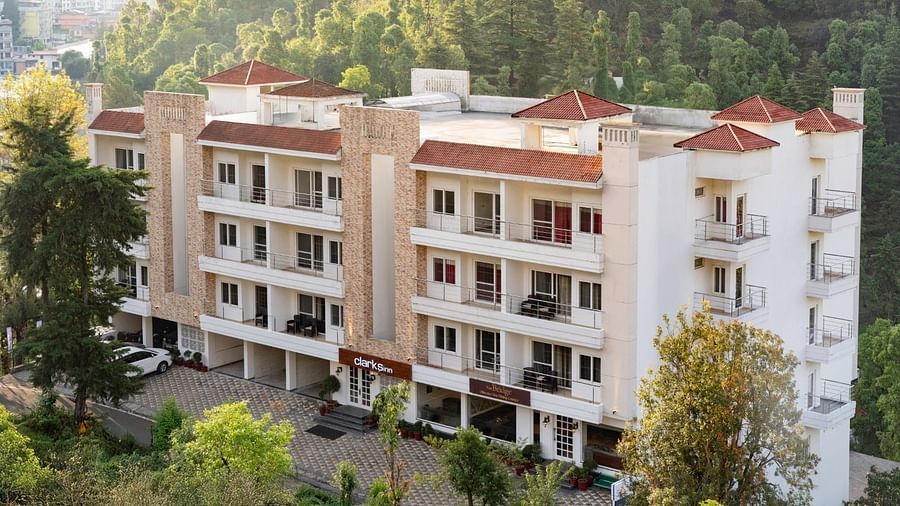 Facade of Clarks Inn, Near Kainchi Dham in Bhowali, nestled among trees with a view of surrounding hills.