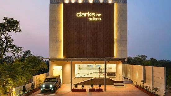 The hotel’s illuminated exterior at dusk, with golden lighting, a luxury car parked outside, and a warmly lit entrance – Clarks Inn Suites, Near Taj Mahal.