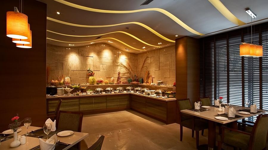An image of a restaurant featuring several sets of tables and chairs at each corner and there are ceiling lights as well as lamps lighting up the area at Adarsh Hamilton