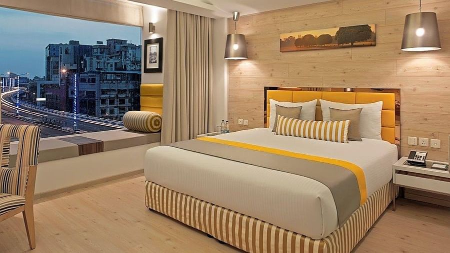 a posh and tidy DELUXE ROOM at Barsana Boutique Hotel Kolkata - designed with soft hues of yellow and white along with a floor-to-ceiling window offering a city view