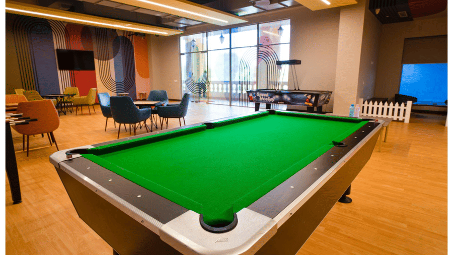 A modern indoor lounge and games area featuring a green snooker table, comfortable seating, and a football table in a bright room at Apartel by Aarin, Oragadam.
