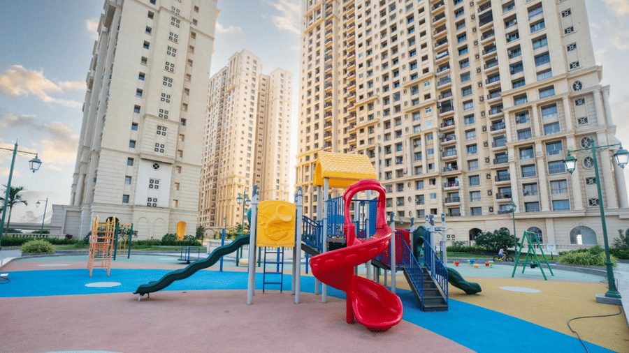 A colourful children’s play area with slides and climbing frames, situated in the courtyard of a modern, high-rise residential apartment complex at Apartel by Aarin, Oragadam.