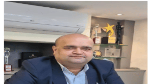 A man in a suit sitting in front of a wall frame during an interview - Lords Hotels & Resorts