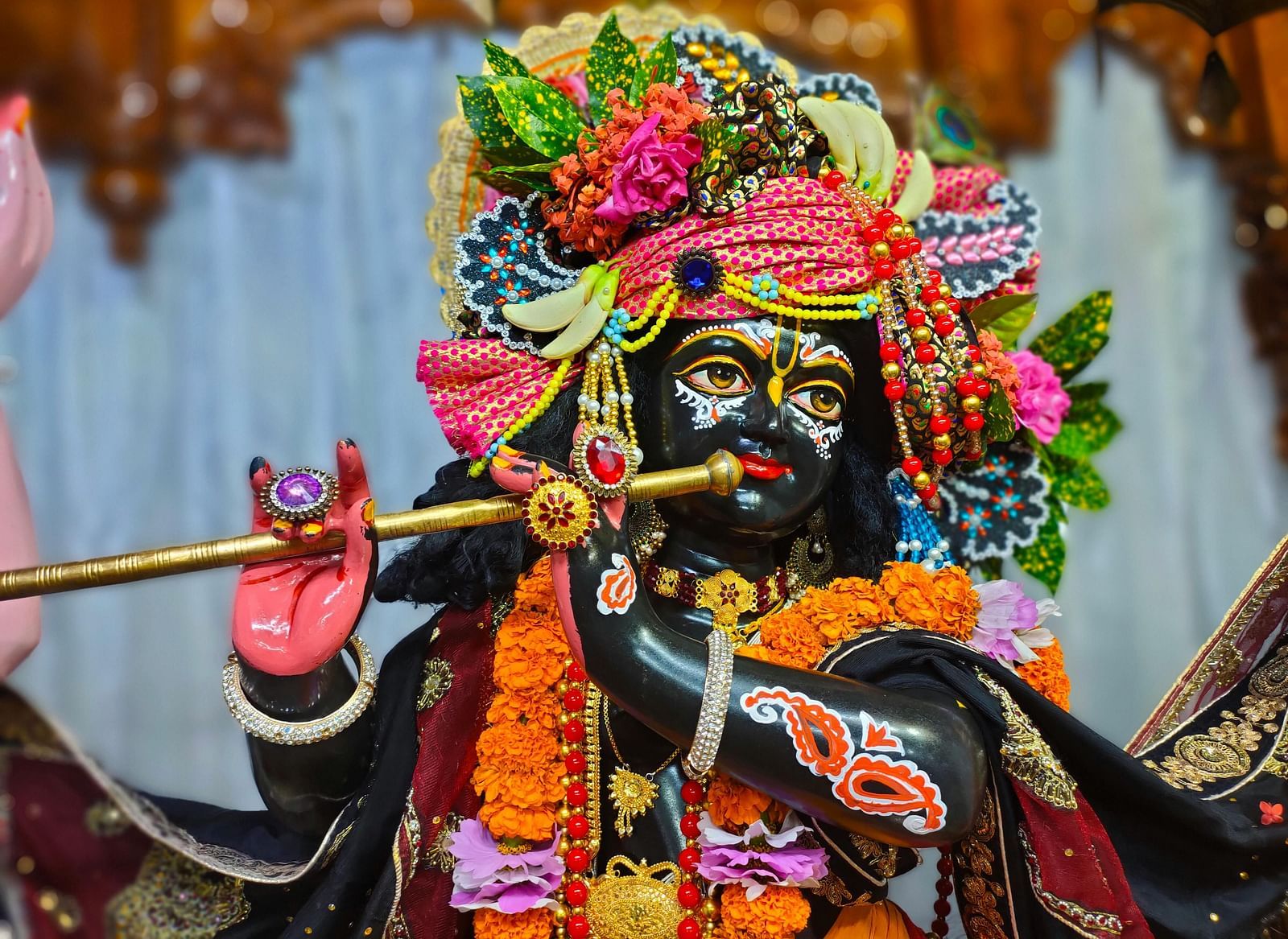 A colourful Hindu deity statue adorned with flowers and jewellery, playing a flute.