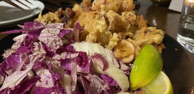 A plate of crispy fried calamari with a side of cabbage and lime wedges