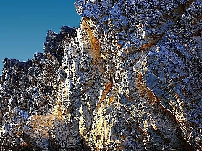 A rugged cliff face meets the ocean under a clear sky.