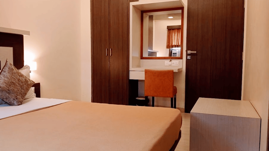 deluxe room view showcasing a beige double bed, wooden closet wardrobe, and a vanity mirror with an orange stool.