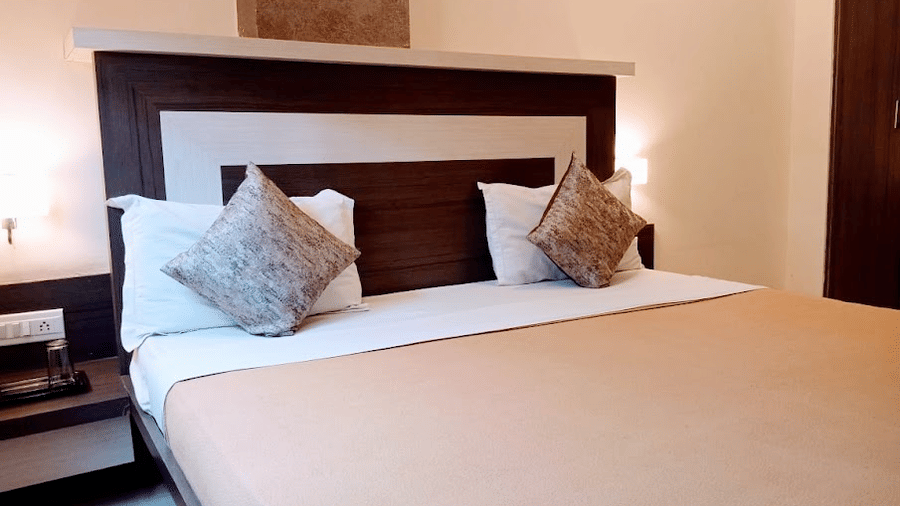 Cozy double bed set with light brown linens, plump white pillows, patterned accent cushions, and bedside tables.