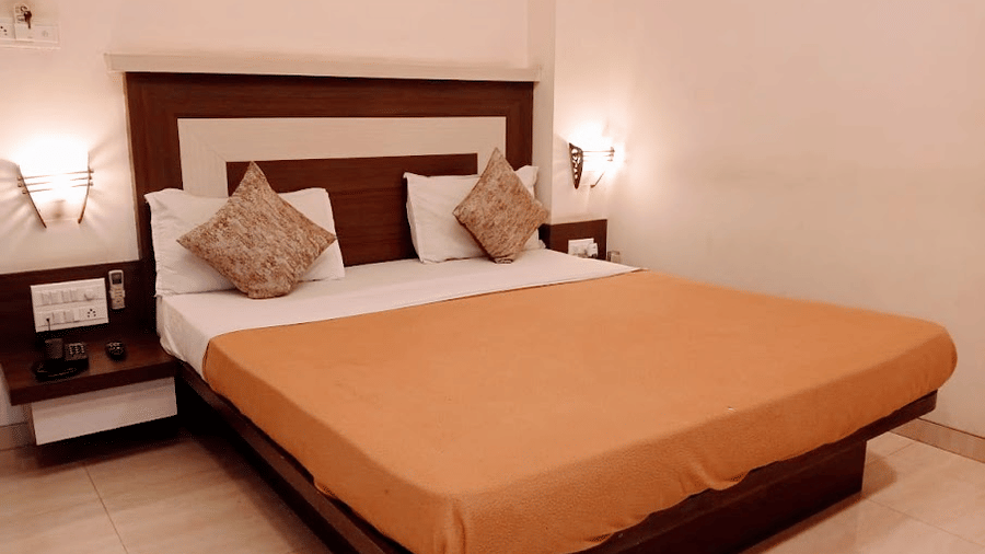 Well-lit deluxe room showing a neatly made double bed with light orange sheets and warm wall-mounted lamps.