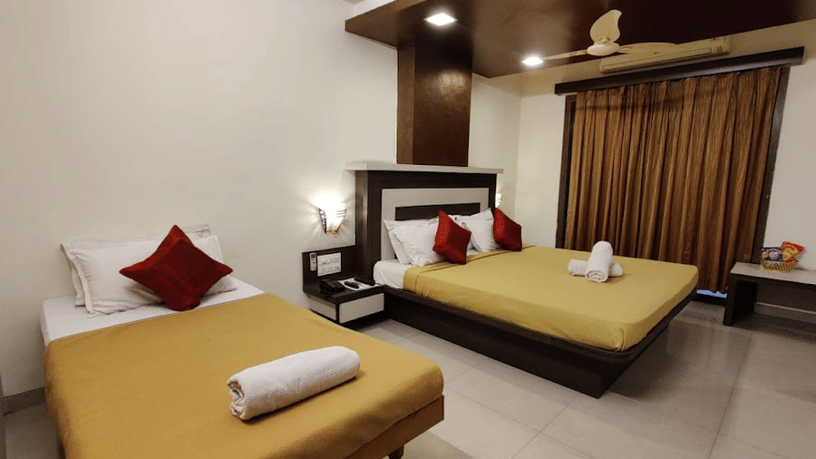 Hotel room setup with a large double bed, an extra single bed, dark brown curtains, and white towels.