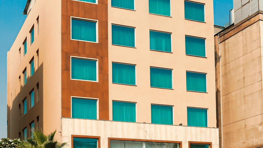 An angular view of the Nemesia City Center Hotel against a blue sky with the entrance being surrounded by trees.