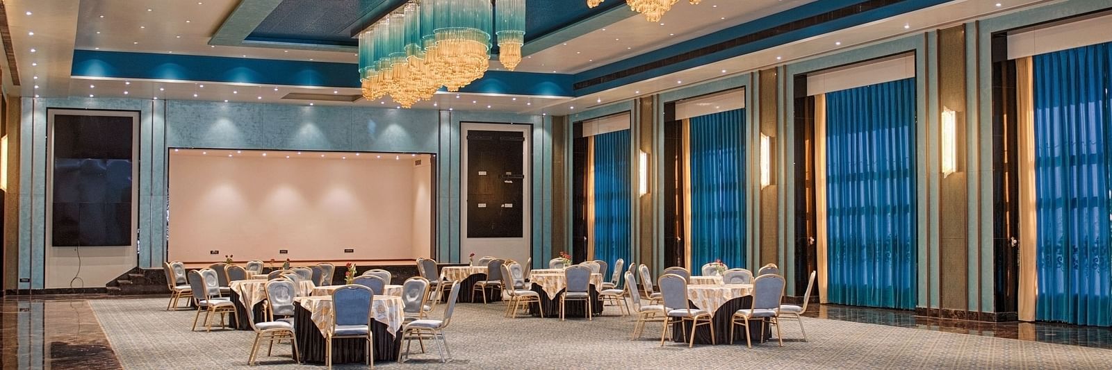 A magnificent banquet with colourful and well designed interiors with long, fancy chandeliers, where the seating is formed in a round table fashion - Crescent Resorts