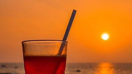 a portrait image of a beverage kept on a table with the setting sun in the background