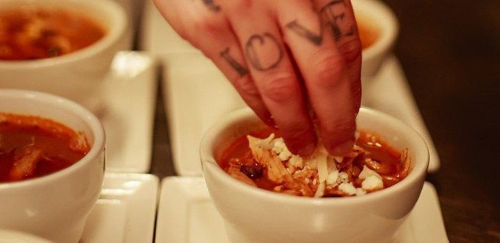 A close-up of a person's hand holding a small dish of food, with other dishes visible in the background.