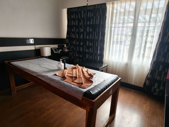 A close-up view of a massage treatment room showing a dark wooden massage table with a brown cushion, ready for a spa service.