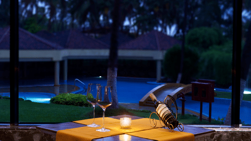 A dining table and chairs, set next to the pool, with candlelight, a bottle of a beverage and two glasses at The Retreat Hotel and Convention Centre.