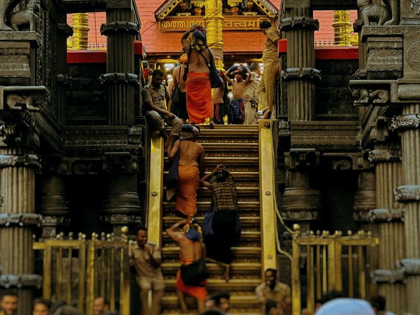 People gathered inside a temple corridor with carved pillars and a decorated shrine visible in the background.