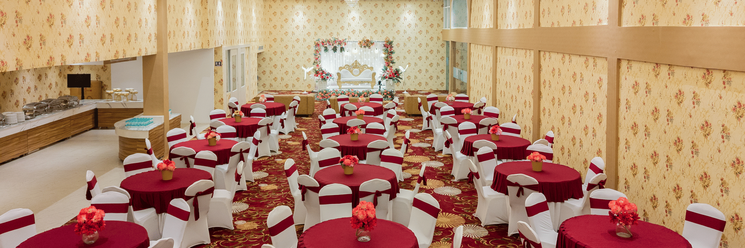 Wide view of banquet hall set up with round tables and red linen at Mango Grove Hotel.