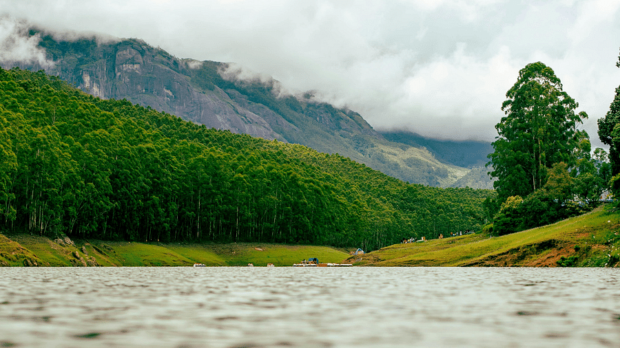 Scenic view of a lake surrounded by lush green hills under a cloudy sky.