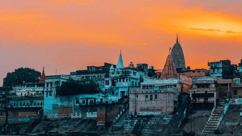Cityscape along a river featuring buildings, temple spires, sky in the background.