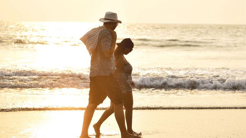 A couple strolls along the glowing shoreline at sunset, casting soft reflections on the wet sand.