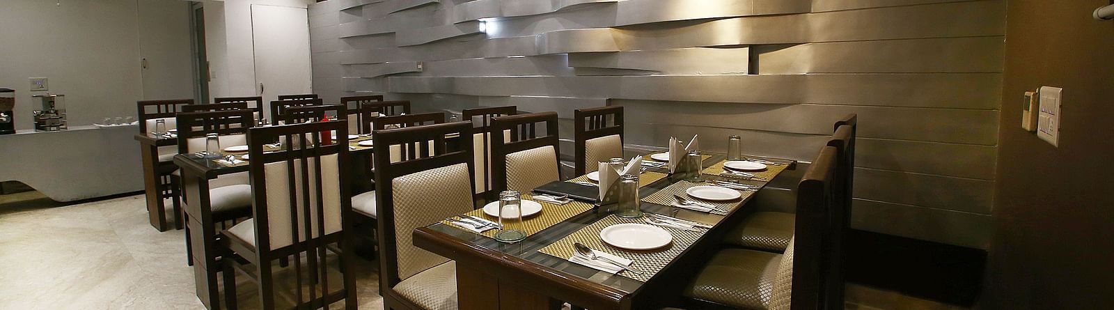 Uniformly placed chairs and tables of mocha and dark shades  in a modern light setting an extremely detailed walls and interior - Hotel Emerald, Chandigarh
