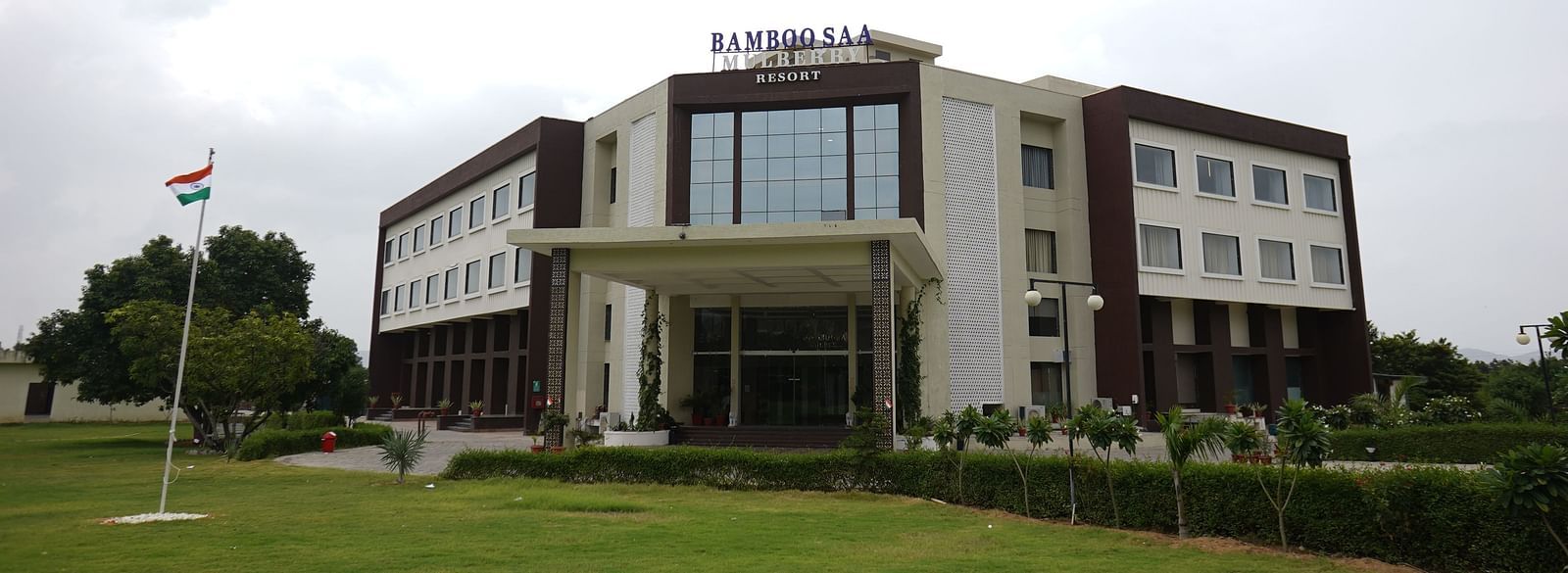 Exterior view of Bamboo Saa Mulberry Resort, Pushkar, Rajasthan featuring a modern building with a light-coloured facade with a lawn in the foreground
