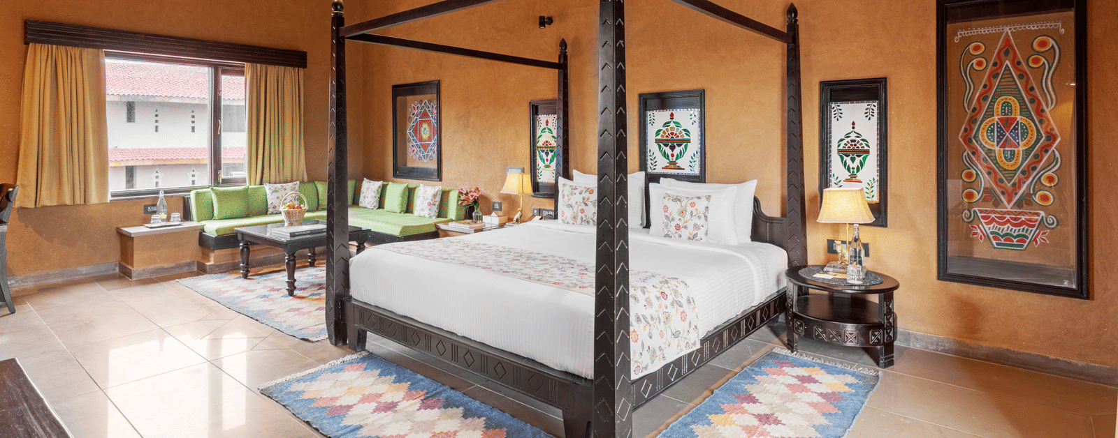 An interior shot of a room featuring a traditional four-poster bed and decor, with a high ceiling and windows at Aamaghati Wildlife Resort.