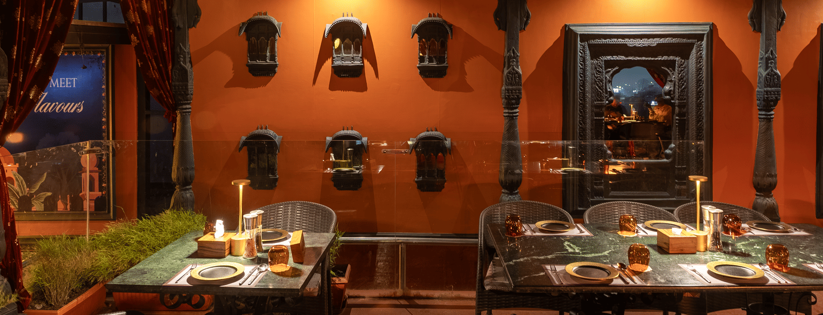 A restaurant interior with warm orange walls, decorative shelves and dining tables with chairs at Infiniti Hotel, Indore.