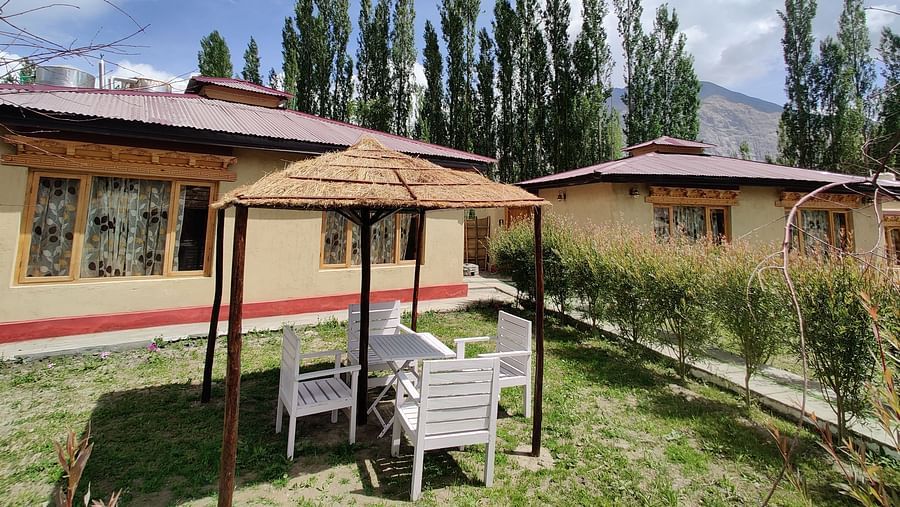 The outdoor seating area of the White Sands Resort, Ladakh featuring chairs and a gazebo, with trees and blue sky overhead.