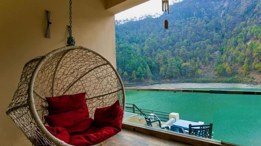 Hanging chair on a balcony with red cushions overlooking a lake and mountains.