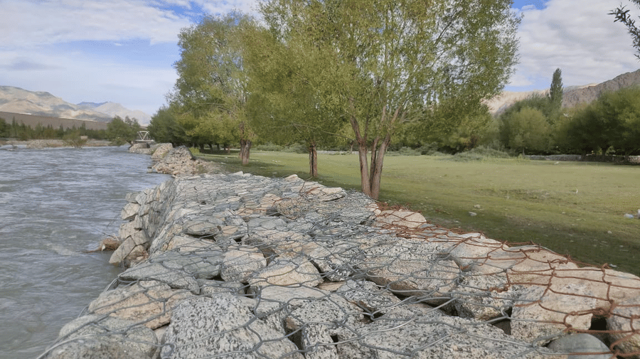 A sturdy stone-paved embankment running alongside a wide, fast-flowing river at Indus Serenity Retreat.