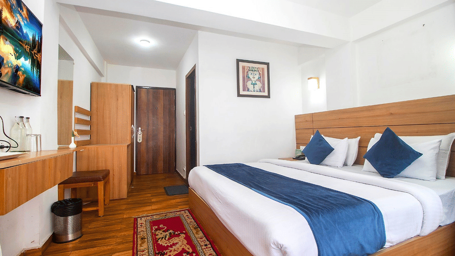 A room with double bed, Framed art work on the wall, TV, Wardrobe, Dustbin, Table and desk with two water bottles on the top at  Central Heritage Resort and Spa (Formerly Fortune ITC Resort) The Mall Road.