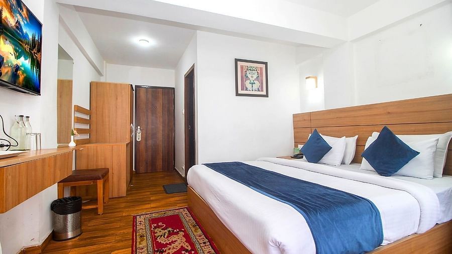 A room with double bed, Framed art work on the wall, TV, Wardrobe, Dustbin, Table and desk with two water bottles on the top at  Central Heritage Resort and Spa (Formerly Fortune ITC Resort) The Mall Road.